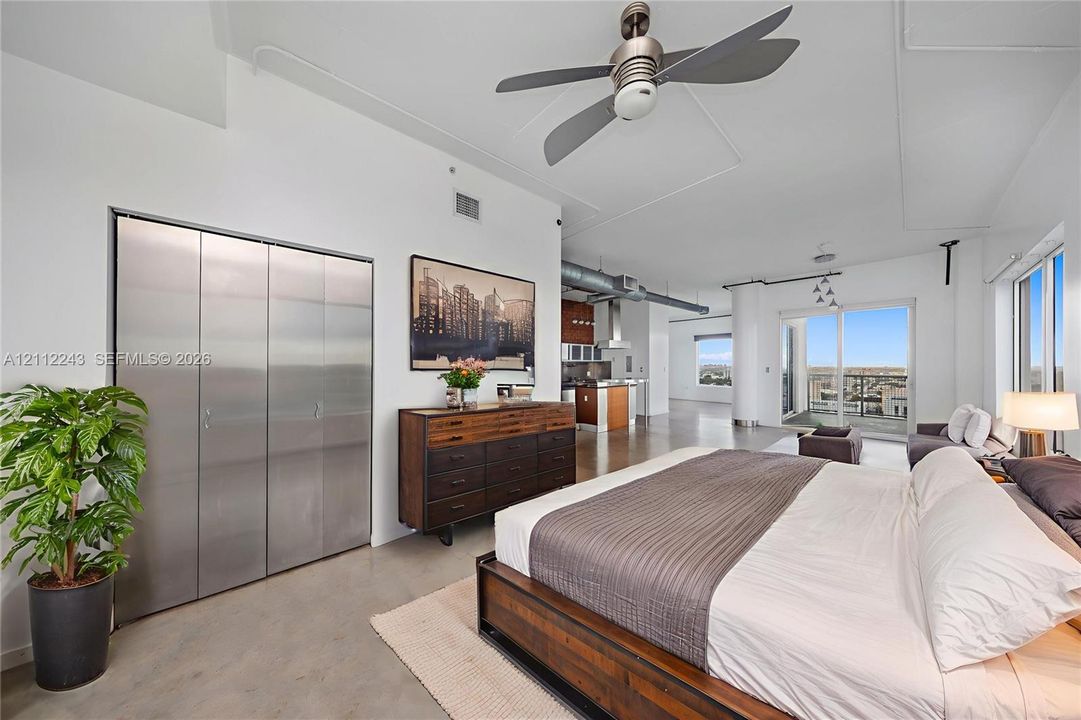 Industrial-style space featuring high ceilings, concrete flooring, stainless steel closet doors, exposed ductwork, and a built-in ceiling fan