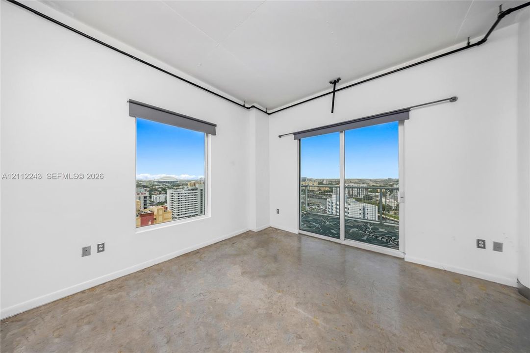 Polished concrete flooring, floor-to-ceiling window, glass sliding door, metal balcony railing, and exposed ceiling conduit