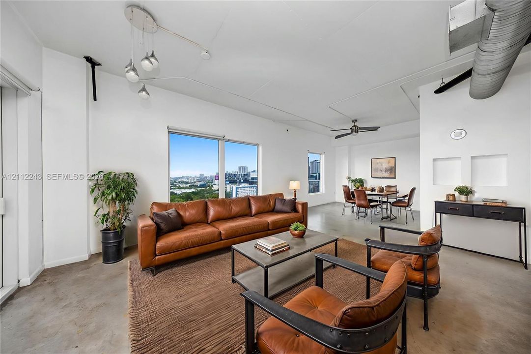 Open-concept interior featuring industrial exposed ductwork, polished concrete flooring, soaring ceilings, large-scale windows, and built-in wall niches