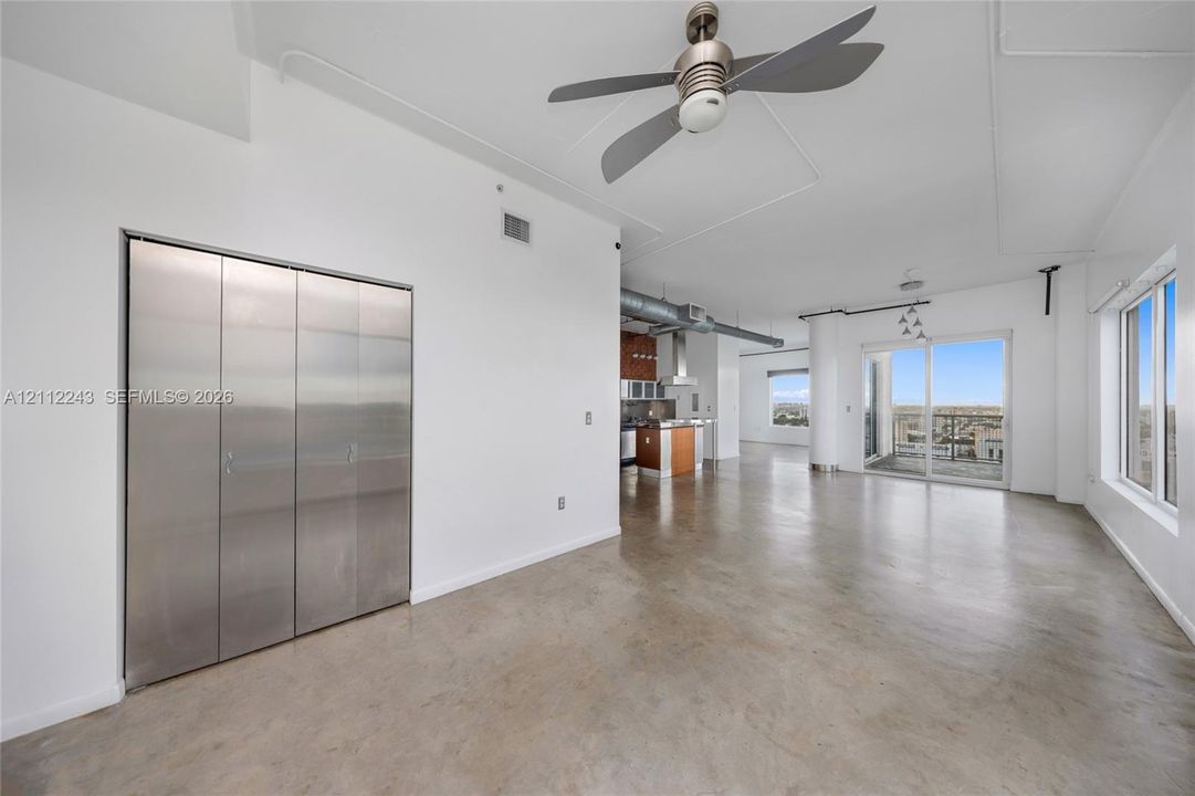 Polished concrete flooring, floor-to-ceiling metal-clad closet doors, industrial-style exposed ductwork, and sliding glass doors with exterior balcony access