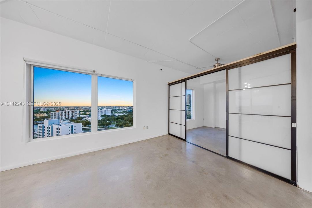 Polished concrete flooring, expansive windows with cityscape backdrop, and floor-to-ceiling sliding panels with opaque glass inserts