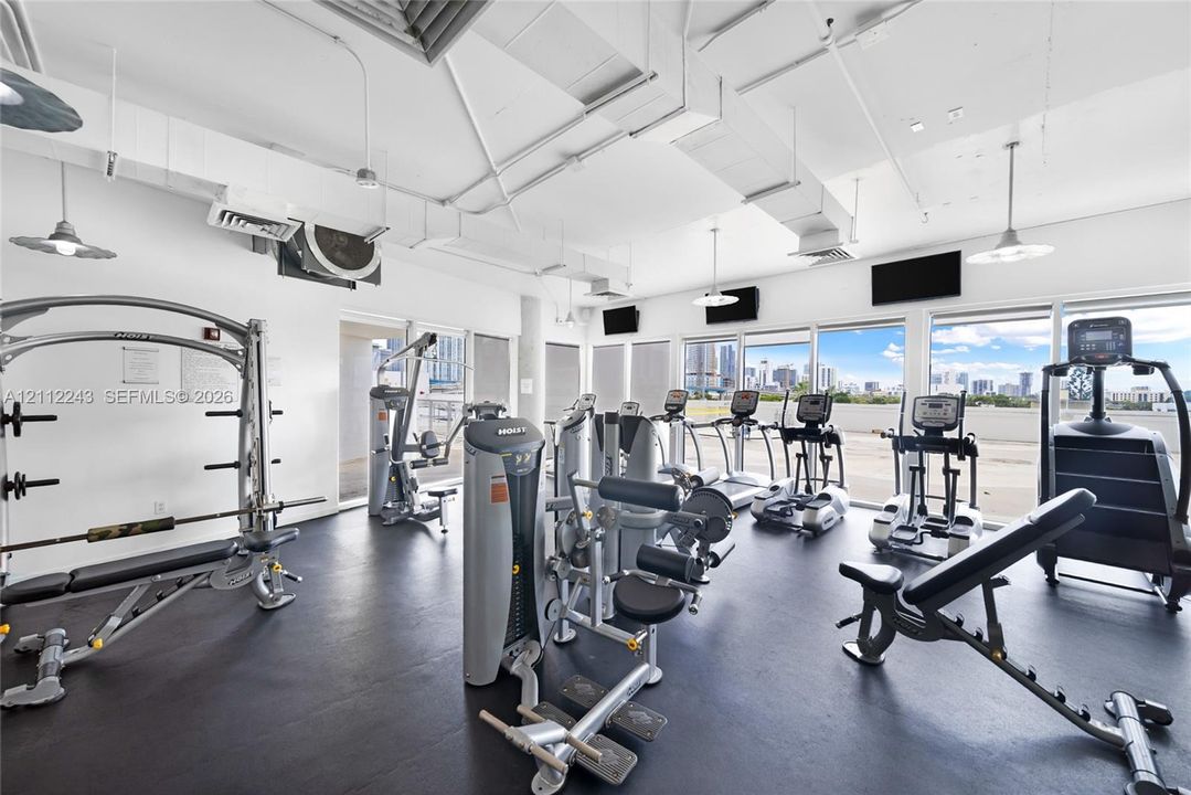 Fitness facility featuring industrial-style exposed ductwork, rubberized flooring, and expansive floor-to-ceiling windows