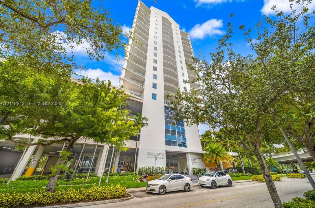 High-rise residential building featuring white stucco facade, tiered glass-railed balconies, and floor-to-ceiling blue-tinted windows