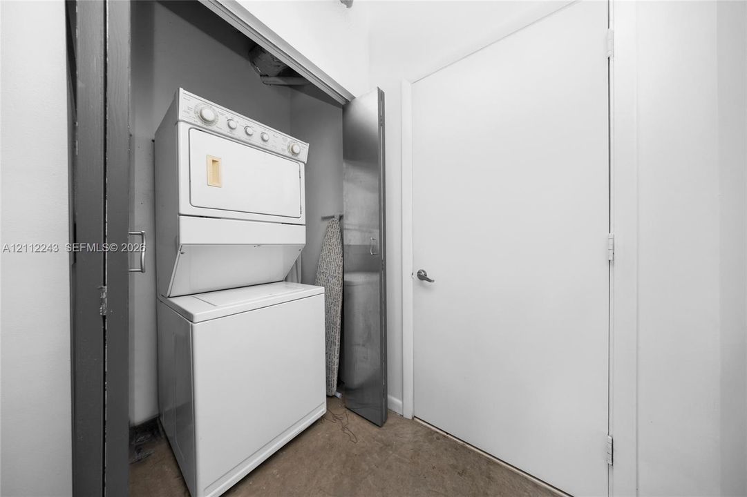 Laundry closet featuring a stackable white washer and dryer unit, solid-core white door, and neutral flooring