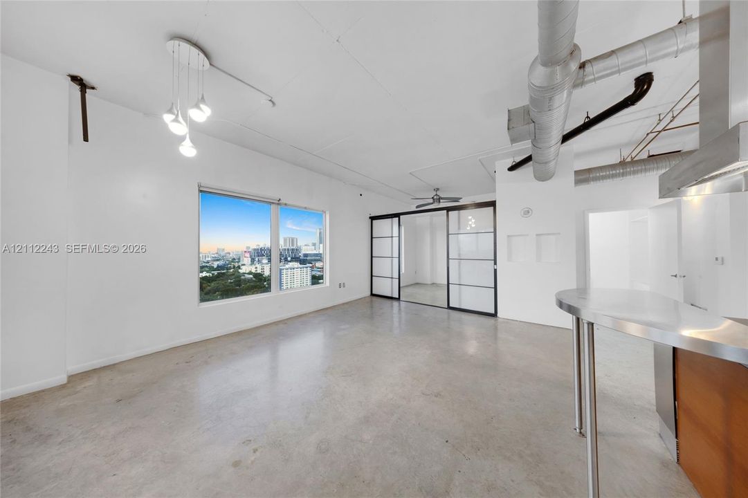 Industrial-style loft featuring polished concrete flooring, exposed ductwork, sliding glass-paneled room dividers, a stainless steel breakfast bar, and multi-light pendant fixture