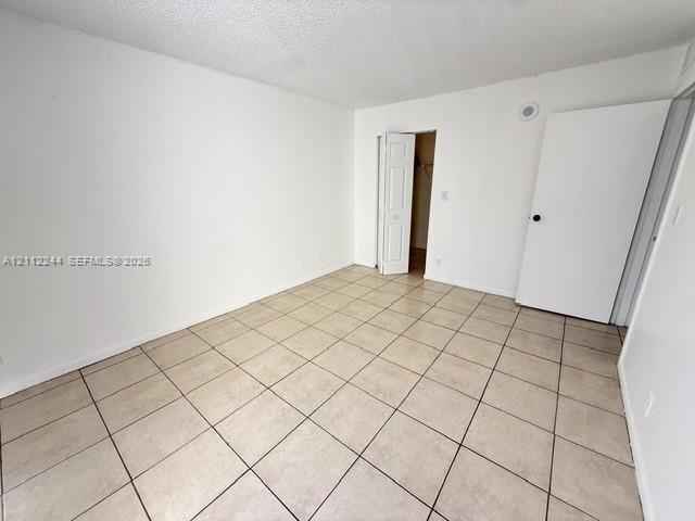 Neutral-toned floor tiling, textured ceiling, solid core swing door, and bifold closet door