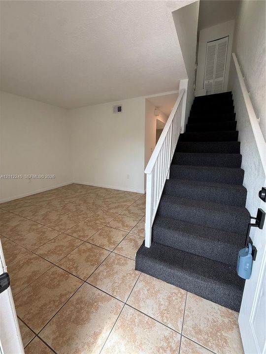 Ceramic tile flooring, white-painted interior walls, and a staircase featuring a white-painted wooden balustrade and charcoal-colored carpet