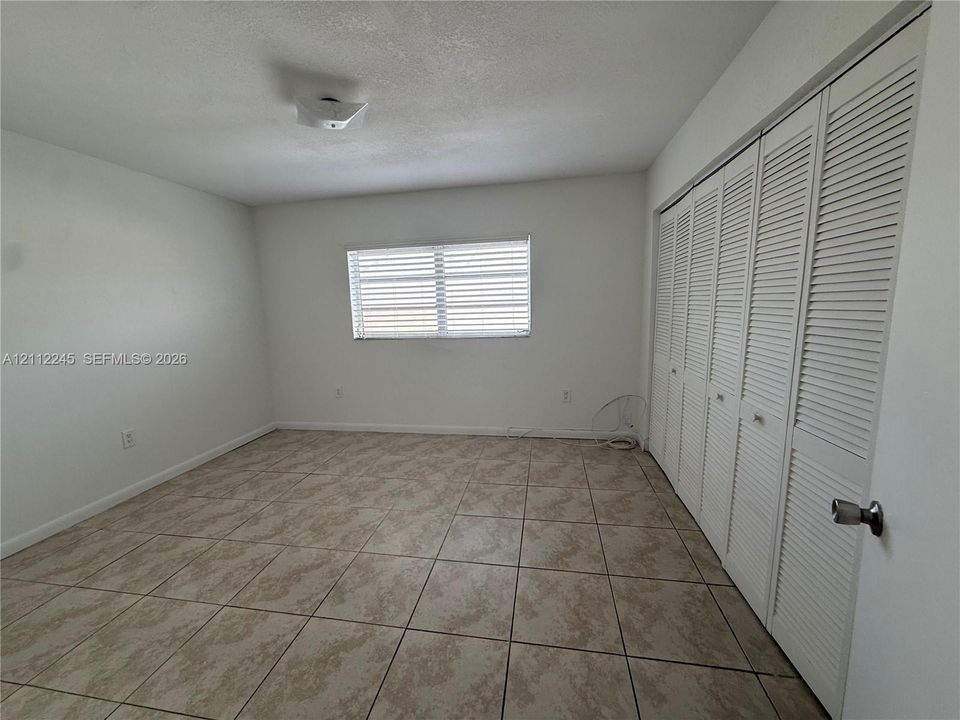 Neutral-toned ceramic tile flooring, multi-pane window with horizontal blinds, and floor-to-ceiling bi-fold closet doors with louvered panels