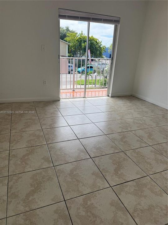 Large-format neutral tile flooring throughout with sliding glass door access to an exterior balcony featuring metal railings and terra-cotta-style flooring