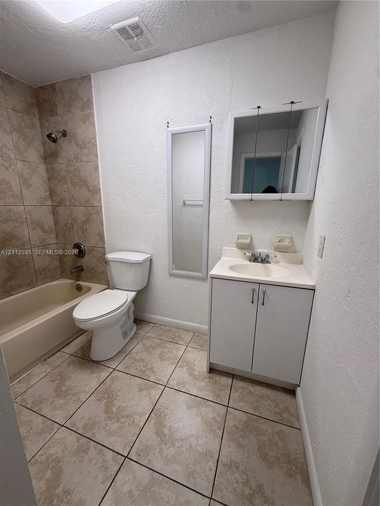 Bathroom featuring ceramic tile flooring, a tub-shower combination with floor-to-ceiling tile surround, a built-in vanity with integrated sink, and a wall-mounted medicine cabinet