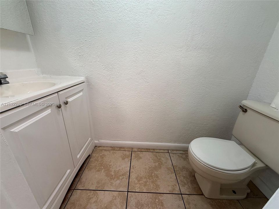 White vanity cabinet with integrated countertop, ceramic sink, porcelain toilet, and neutral tile flooring