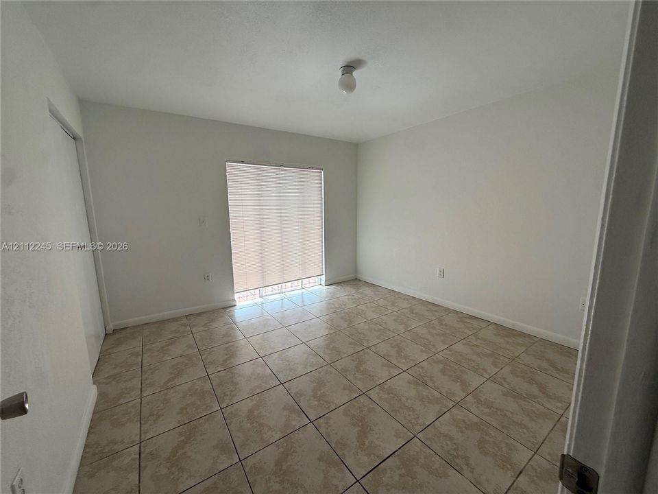 Neutral interior space featuring large-format ceramic tile flooring, a sliding glass door, and overhead lighting