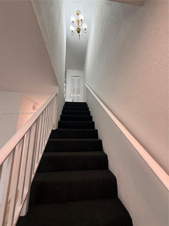 Staircase featuring dark carpeting, white handrail, vertical balusters, and overhead multi-light fixture