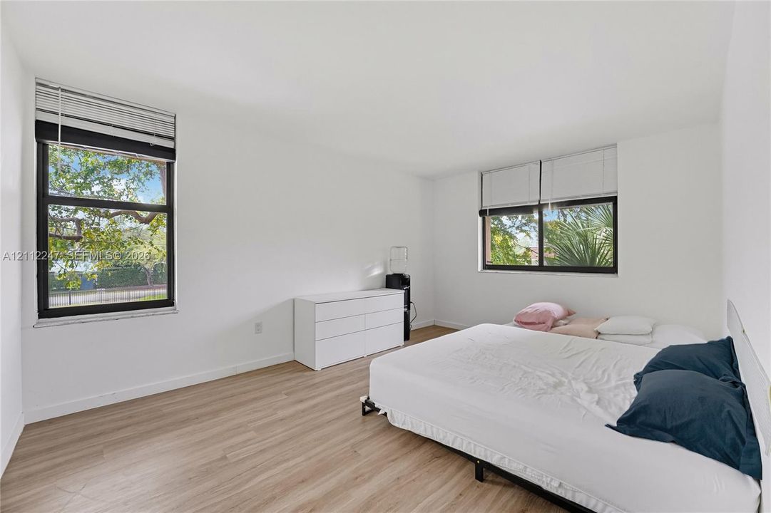 Neutral interior featuring light-tone wood-finish flooring, dual windows with dark frames, and integrated window blinds