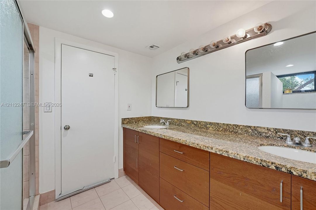 Dual-sink vanity with stone countertops, wooden cabinetry, two wall-mounted mirrors, and tiled flooring