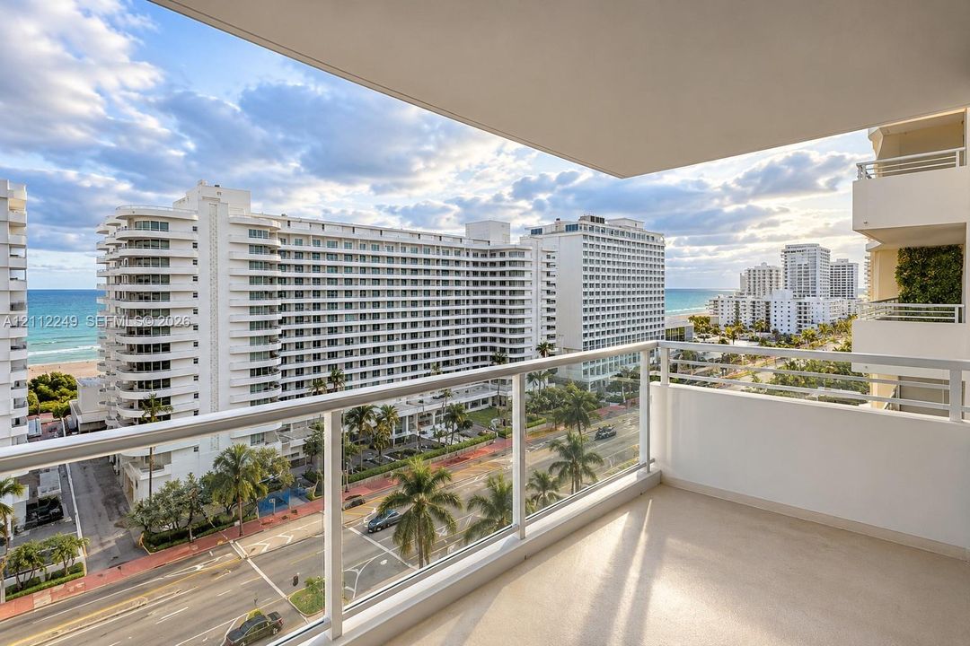 Private balcony featuring a glass-panel railing and concrete flooring, overlooking the ocean and urban landscape