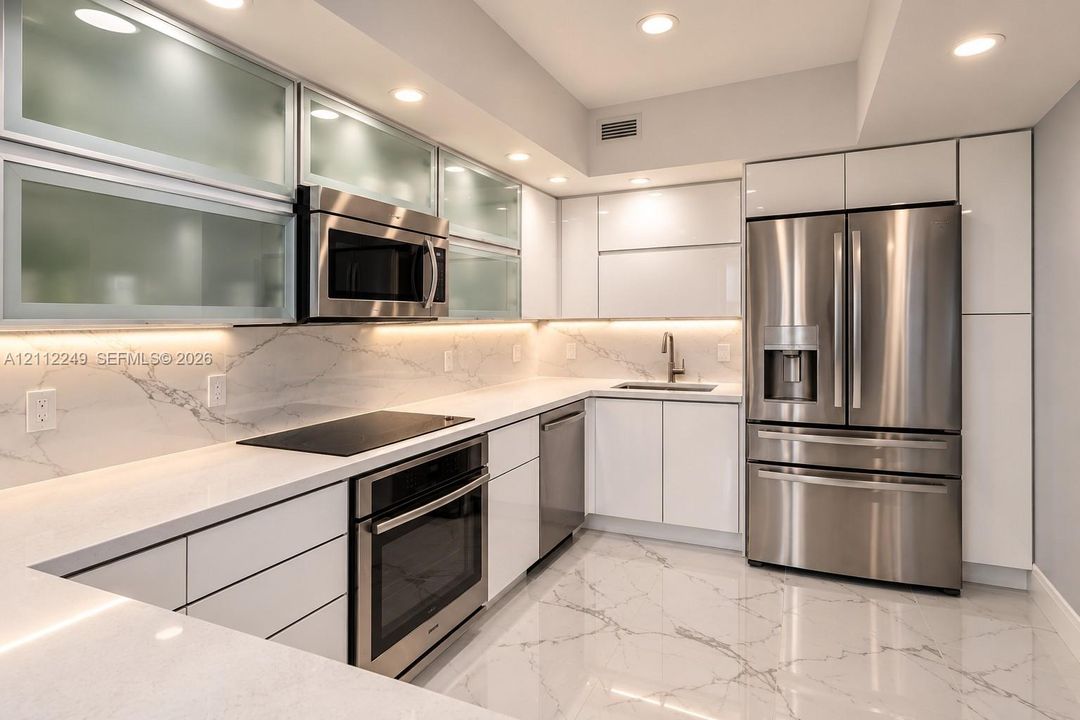 Modern kitchen featuring high-gloss cabinetry, upper glass-front display cabinets, stone-surfaced countertops, integrated under-cabinet lighting, and stainless steel appliances