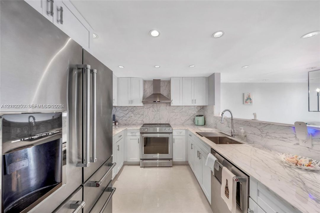 Kitchen featuring white cabinetry, stone-patterned backsplash, stainless steel appliances, and stone-patterned countertops with an integrated sink and gooseneck faucet