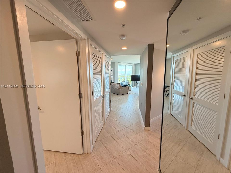 Hallway featuring large-format tile flooring, recessed ceiling lighting, louvered-panel closet doors, and a full-length mirrored door