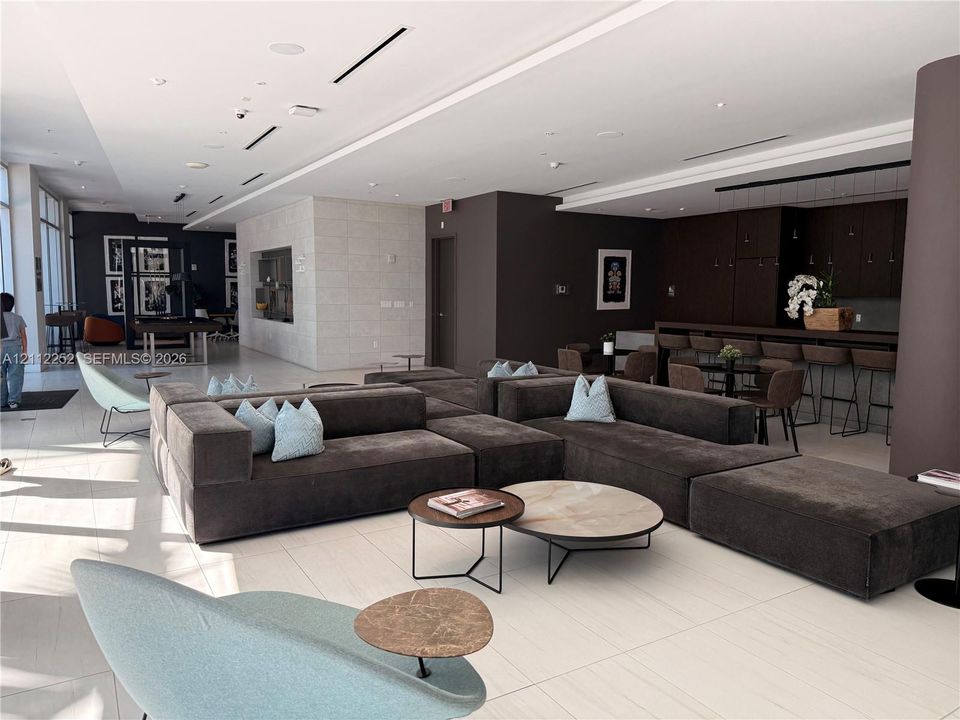 Open-concept interior featuring large-format tile flooring, recessed ceiling lighting, stone-textured accent wall, and a built-in dark wood cabinetry bar