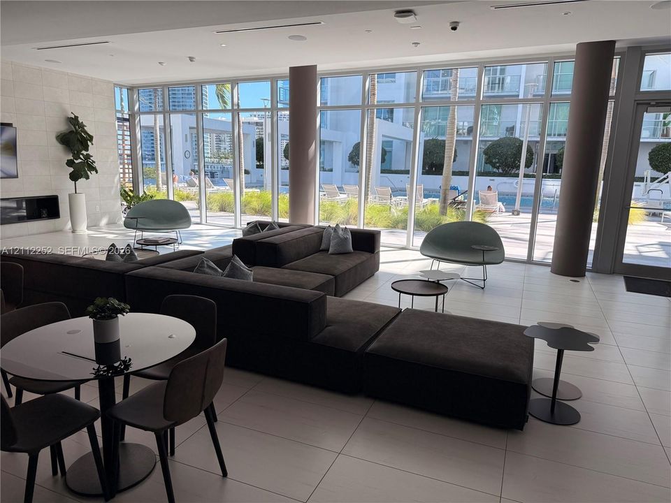 Common area featuring floor-to-ceiling windows, large-format tile flooring, built-in horizontal fireplace, and cylindrical support columns