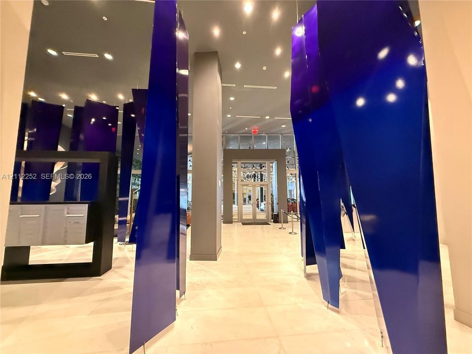 Grand lobby entrance featuring high-gloss geometric blue panels, large-format tile flooring, recessed ceiling lighting, and built-in metallic mailboxes