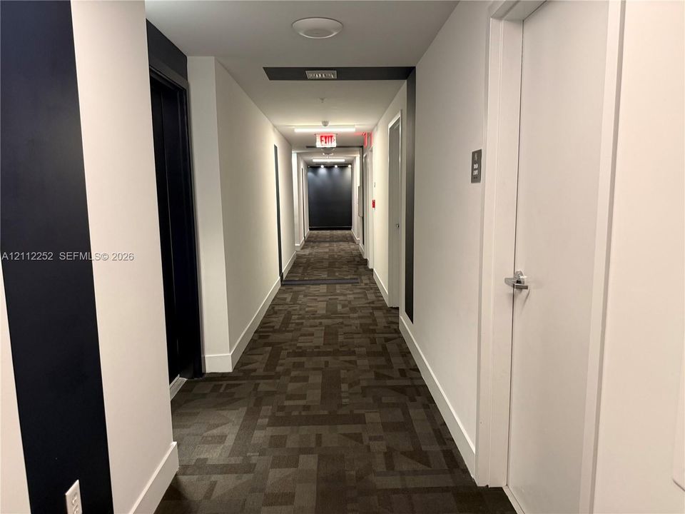 Hallway featuring patterned carpet, high-contrast dark accent walls, white interior doors with satin nickel hardware, and recessed ceiling lighting