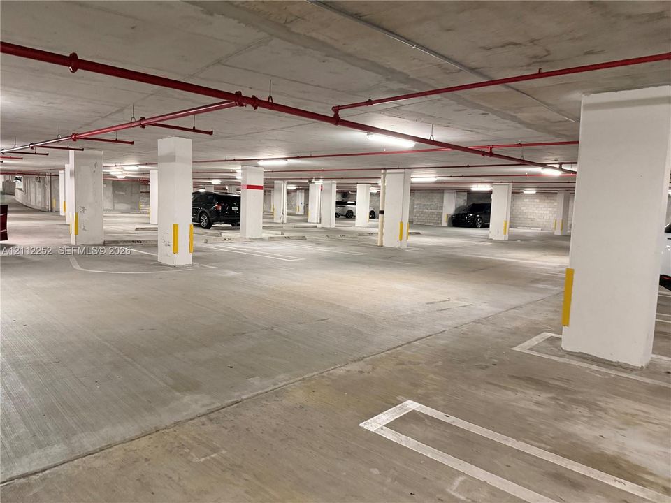Covered parking garage with a concrete floor, concrete support columns, and overhead sprinkler system