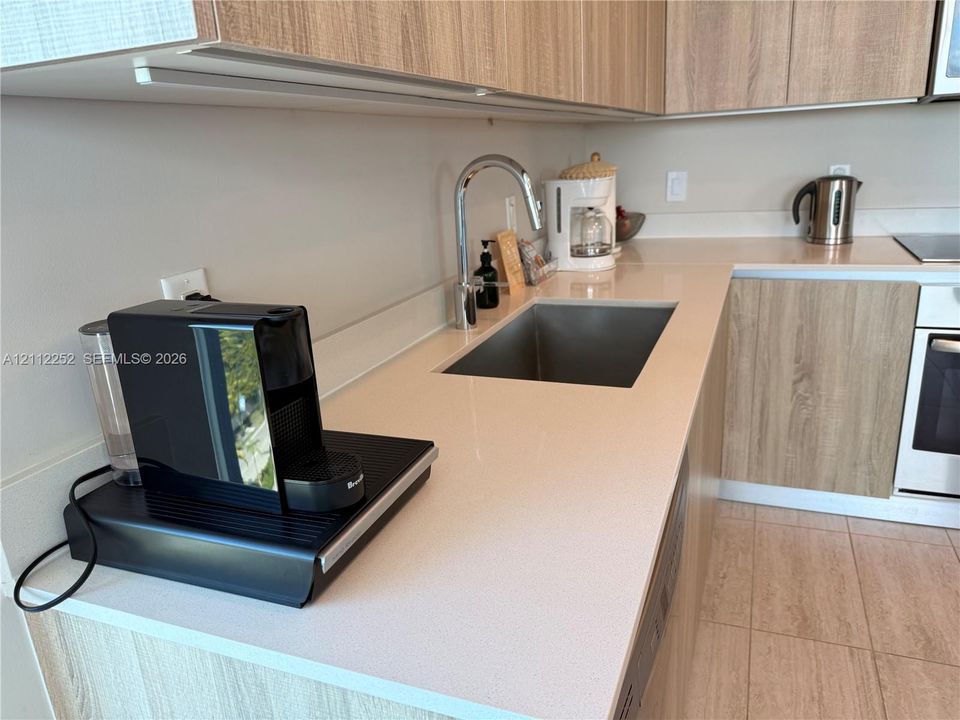 Kitchen featuring light wood-finish cabinetry, solid-surface countertops, an undermount stainless steel sink with a high-arch faucet, and an integrated oven