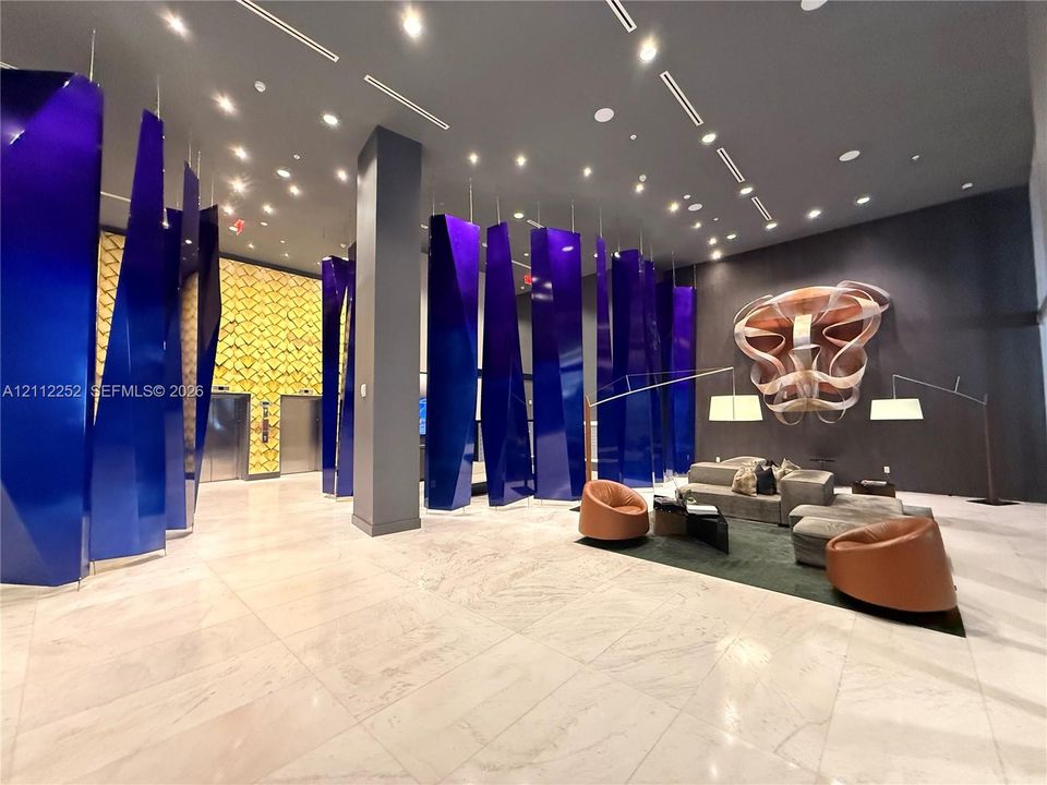 Lobby featuring polished stone flooring, custom blue geometric architectural panels, recessed lighting, and intricate metallic wall-mounted sculpture