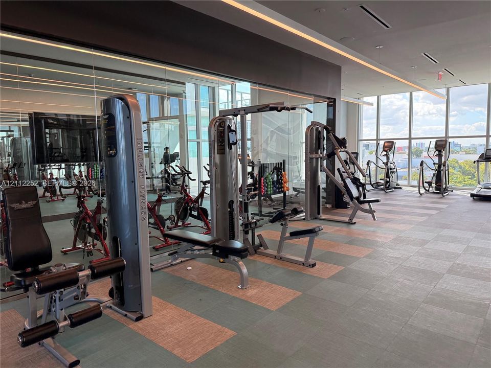 Fitness center featuring floor-to-ceiling windows, mirrored walls, recessed linear lighting, and large-format tiled flooring