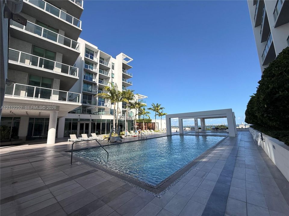 Swimming pool with tiled decking, poolside cabana, and multi-story architectural exterior featuring glass-paneled balconies