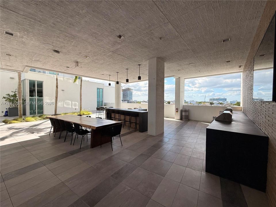 Covered outdoor terrace featuring large-format tile flooring, a built-in outdoor kitchen with a dark countertop, recessed ceiling lighting, and pendant fixtures