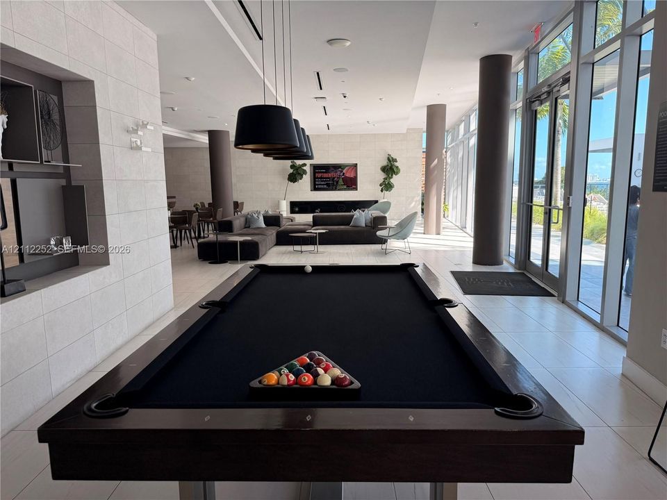 Common area featuring large-format tile flooring, floor-to-ceiling glass wall panels, built-in recessed shelving, matte black pendant lighting, and a linear fireplace