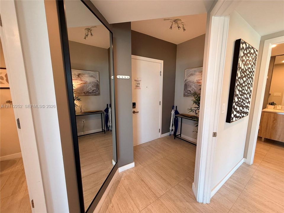 Entryway featuring large-format tile flooring, a floor-to-ceiling wall-mounted mirror with a black frame, and multi-directional overhead track lighting