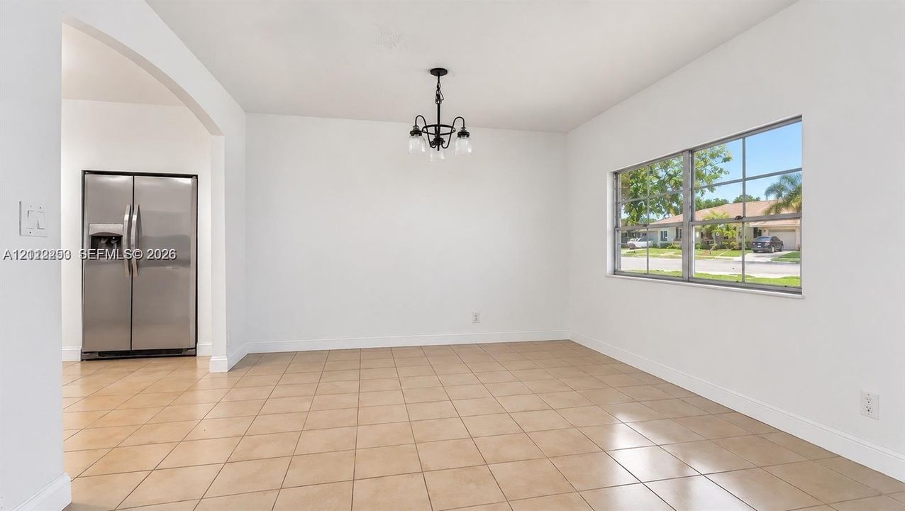 Open interior featuring neutral tile flooring, a multi-pane window, a decorative black metal chandelier, and a stainless steel side-by-side refrigerator