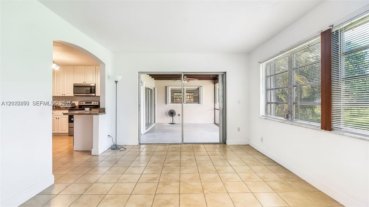 Ceramic tile flooring, arched wall opening, sliding glass doors, horizontal window blinds, and kitchen cabinetry with stone-finish countertops