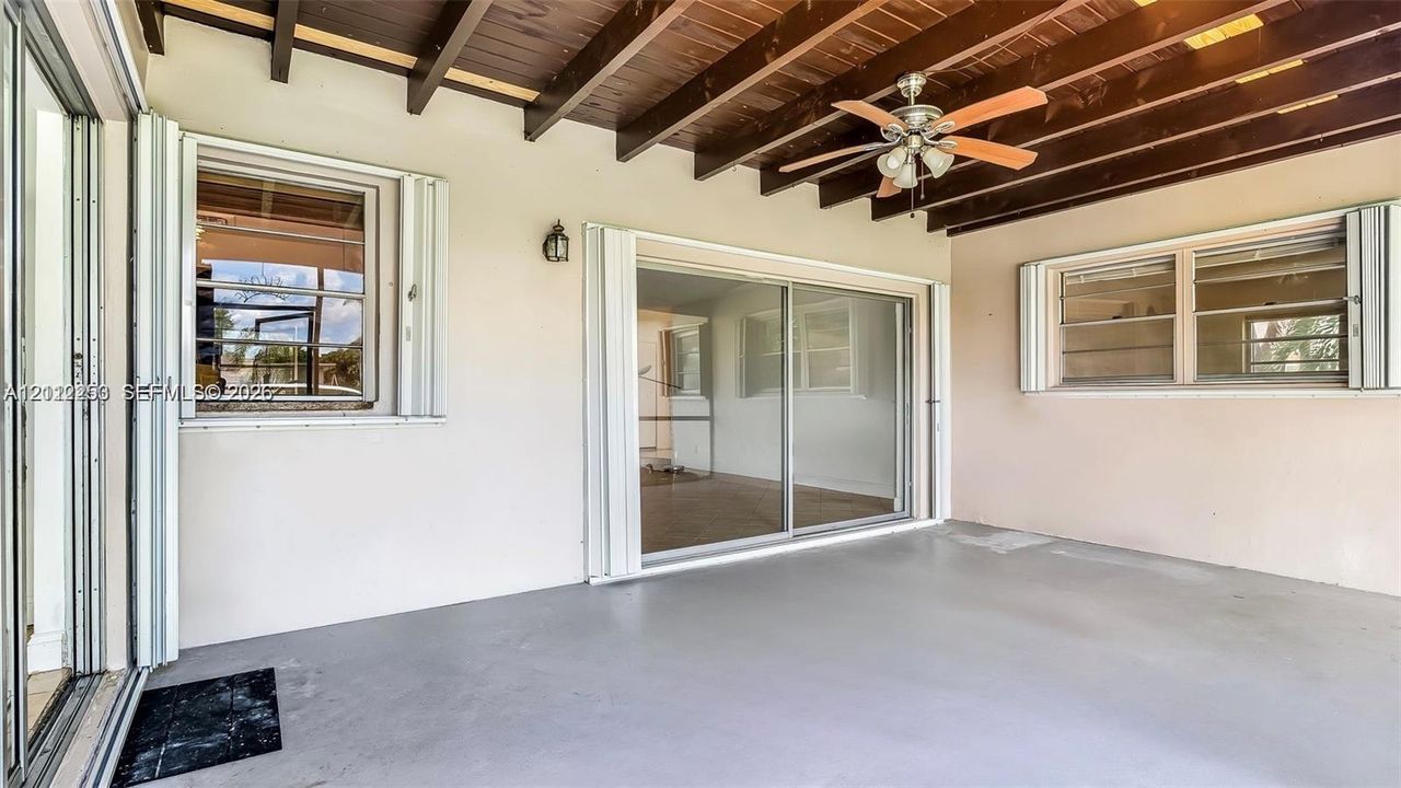 Screened Covered patio featuring an exposed wood-beam ceiling, ceiling fan with integrated lighting, sliding glass door entry, and accordion-style storm shutters