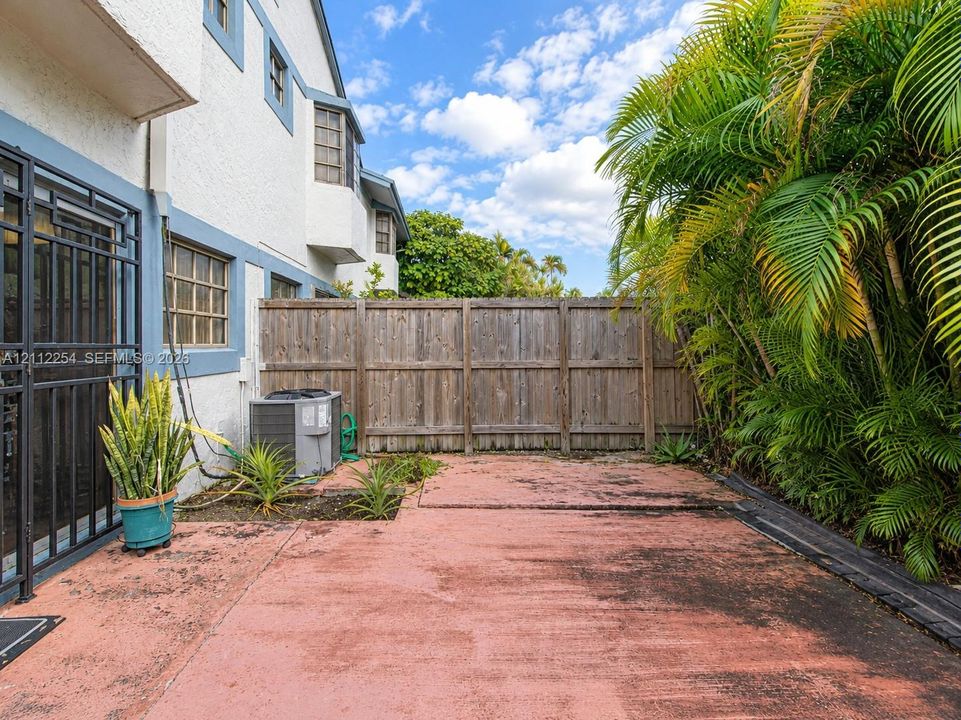 Exterior space featuring a concrete patio, perimeter wood fencing, and mature palm vegetation