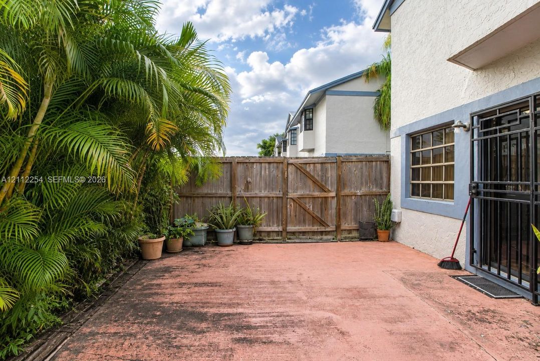 Stucco exterior patio featuring a concrete surface, wood-panel fencing, metal security door, and mature palm trees