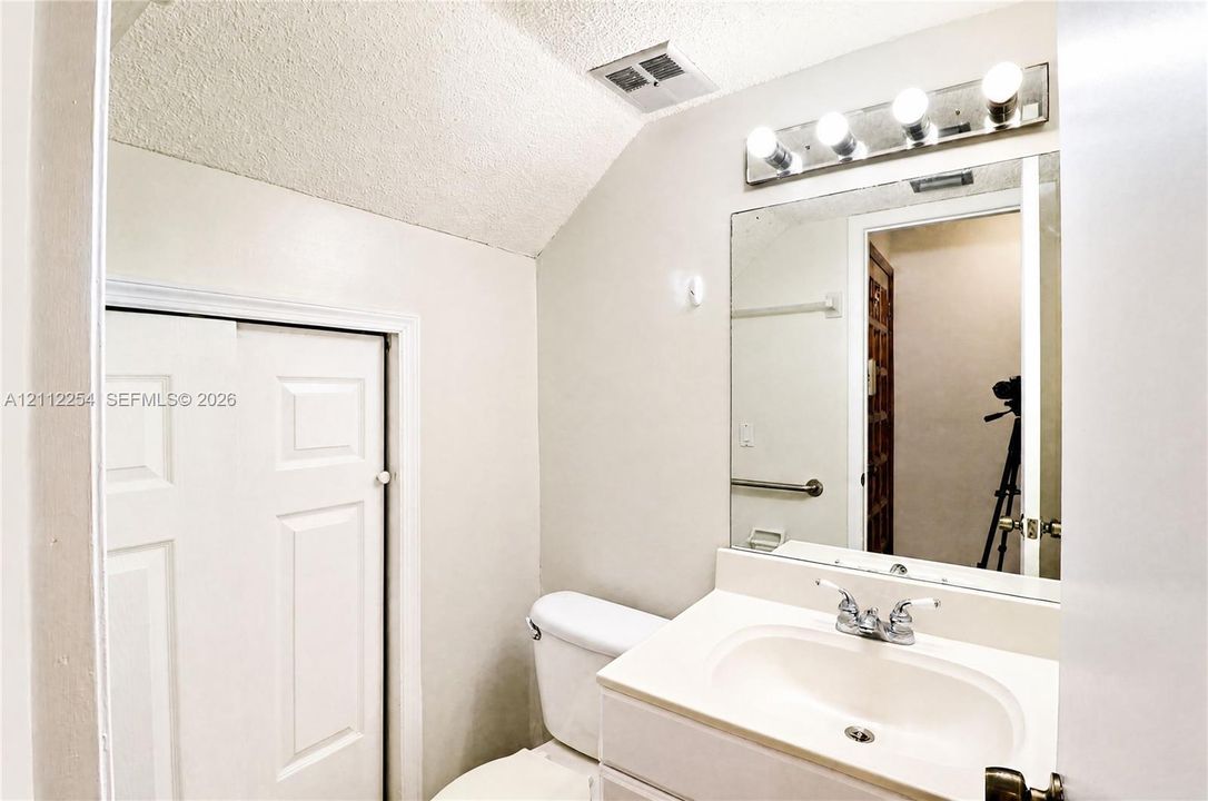 Bathroom featuring a vanity with an integrated sink, polished chrome faucet, rectangular wall-mounted mirror, four-light vanity fixture, and white bi-fold closet doors