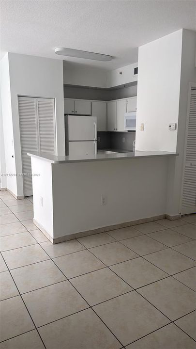 Kitchen featuring a breakfast bar, white cabinetry, integrated appliances, and neutral tile flooring