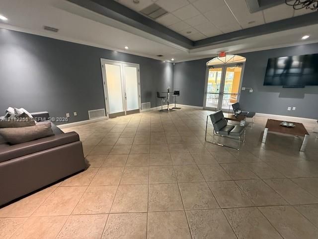 Open-concept room featuring large-format tile flooring, recessed tray ceiling, double French doors with frosted glass, and arched glass-paneled exterior doors