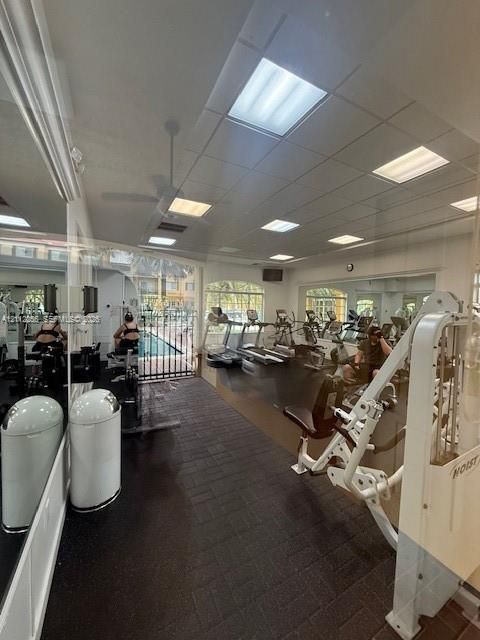 Fitness center featuring wall-to-wall mirrors, recessed drop-ceiling lighting, and dark rubberized flooring
