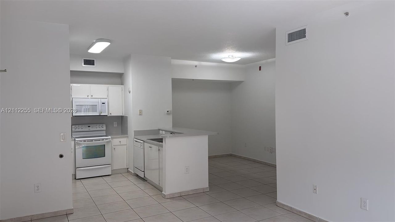 Kitchen featuring white cabinetry, solid-surface countertops, built-in dishwasher, and white appliances, finished with tile flooring