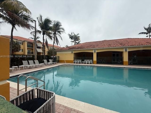Swimming pool featuring a surrounding stone-paver deck, metal railings, and a covered lanai with architectural arches