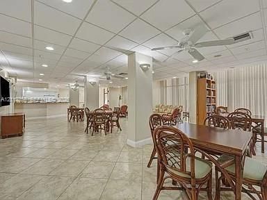 Large communal space featuring ceramic tile flooring, a suspended grid ceiling, recessed lighting, multiple ceiling fans, and a built-in refreshment bar with cabinetry