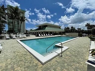 Rectangular swimming pool featuring integrated steps and a metal handrail, surrounded by stone paver decking and mature palm trees