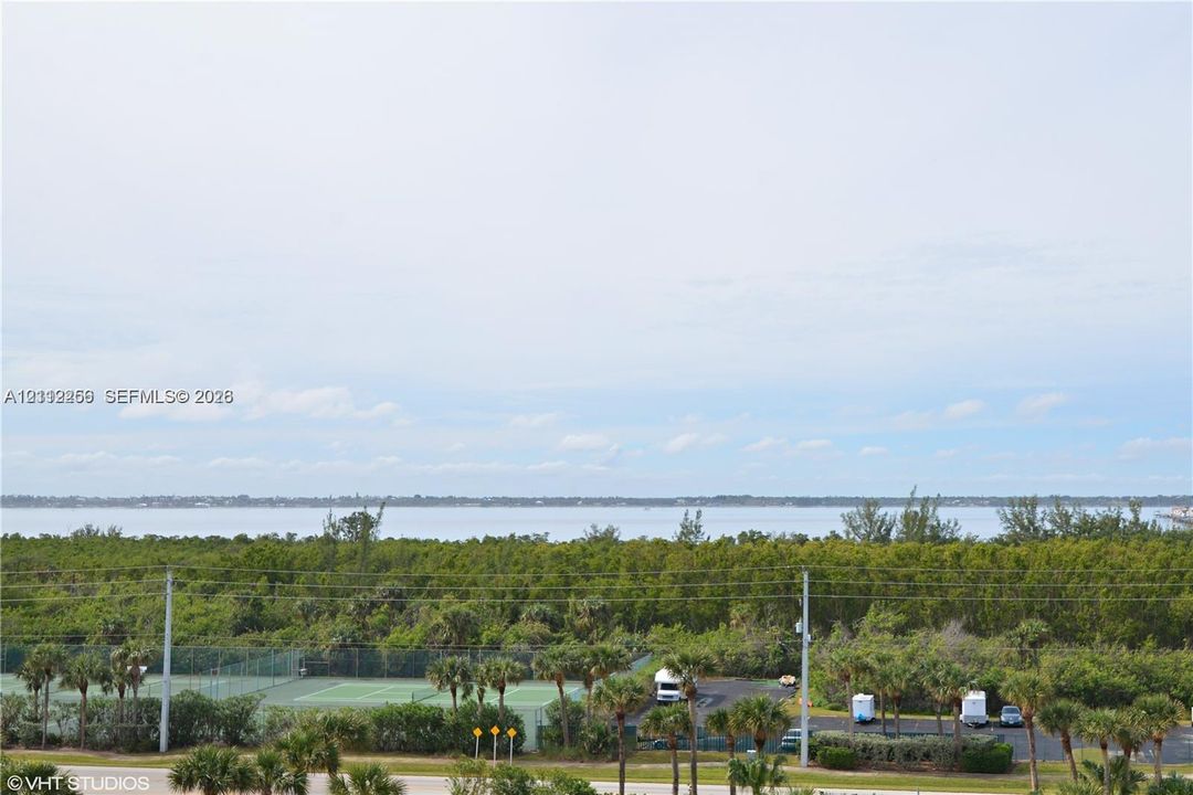Expansive water horizon with mature treeline, featuring an outdoor tennis court and paved parking area
