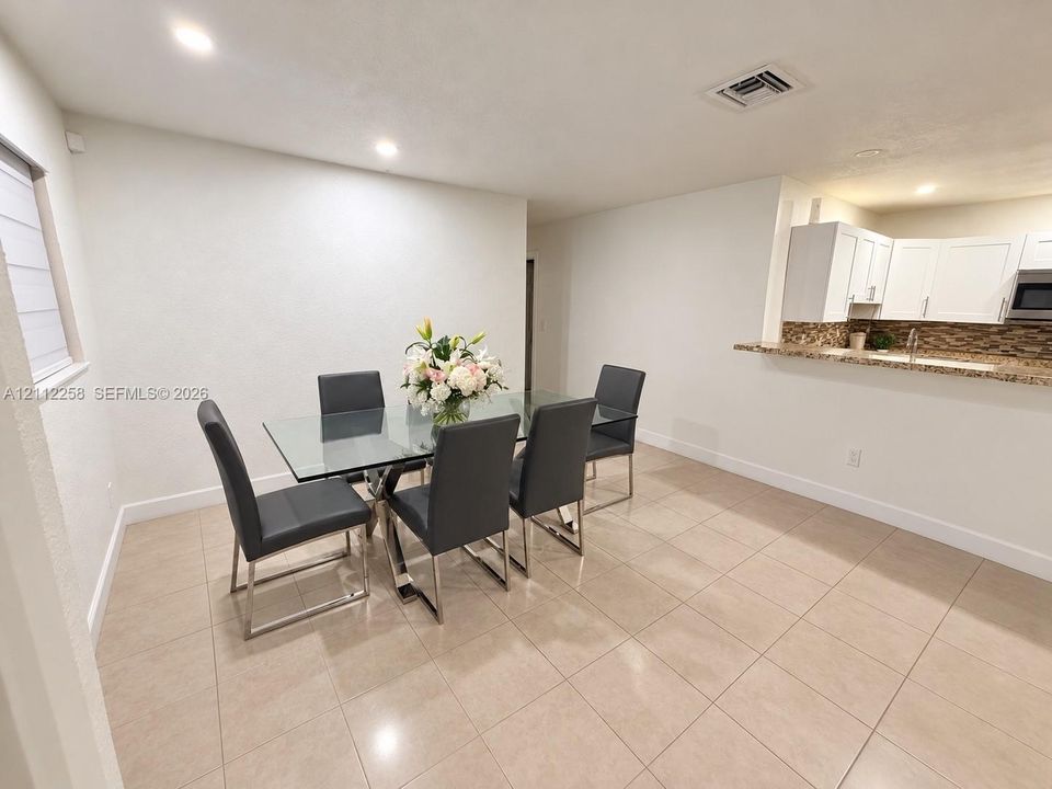 Open-concept space featuring large-format neutral floor tile, white shaker-style cabinetry, a stone-patterned backsplash, and a breakfast bar